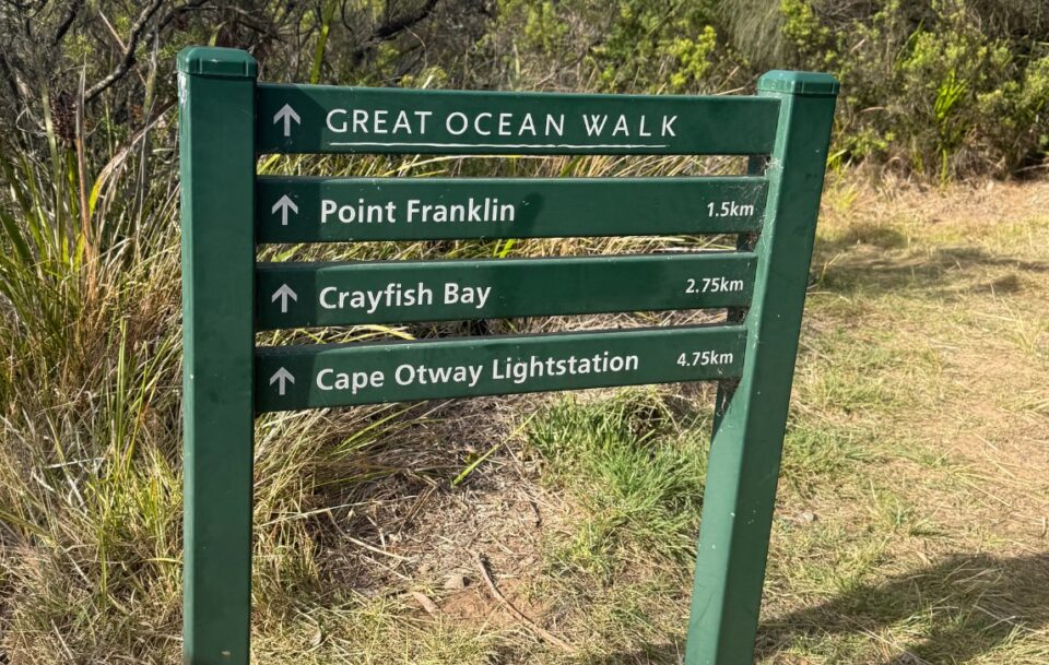 A green wooden sign on the Great Ocean Walk showing the distance to Cape Otway Lightstation and other highlights.