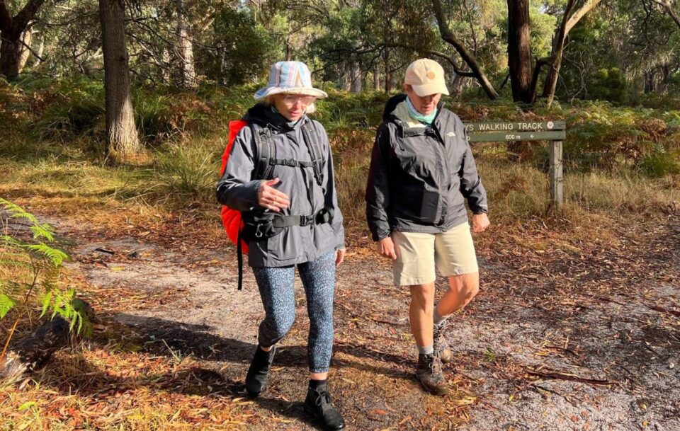 Two hikers on a bushland track with a sign behind them for the Two Bay's Walking Track in the Mornington Peninsula.