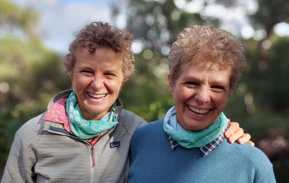 Close up of two older women wearing neck buffs and smiling at the camera