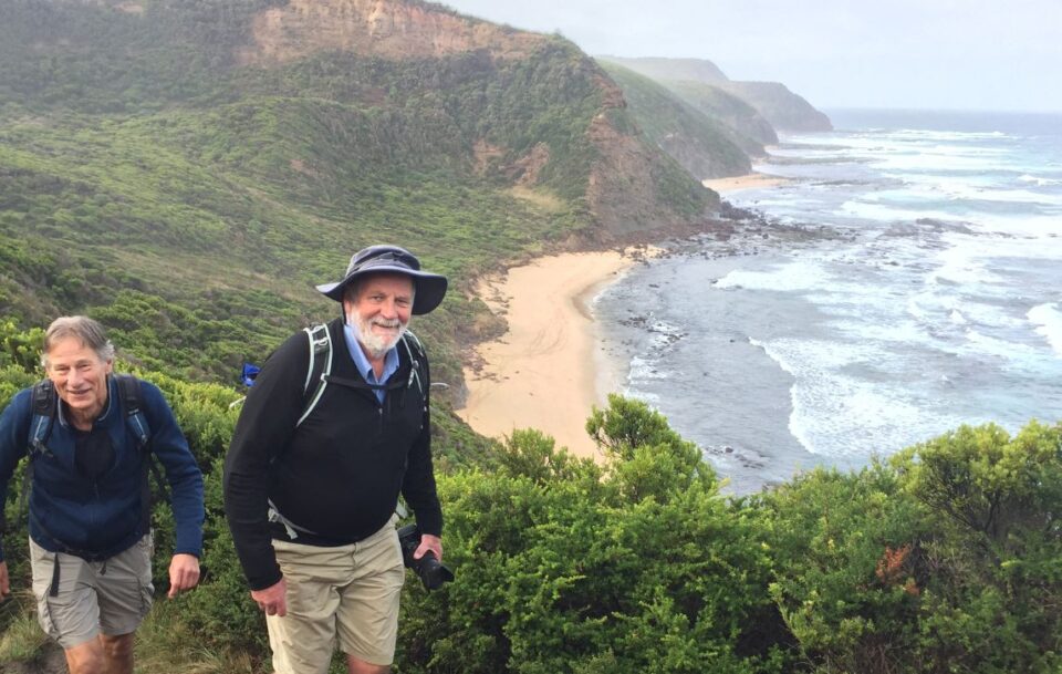 Two male hikers climbing up a path with the coastline and beach in the background