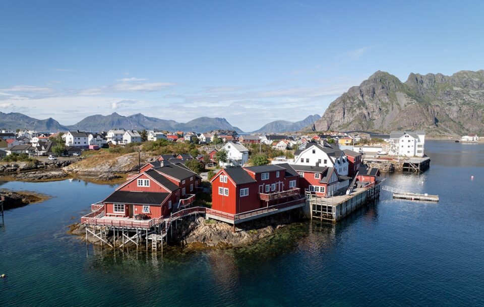 Exterior of a colourful hotel perched on a fjord in the Lofoten Islands in Norway with mountains in the background