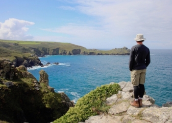 Corwnwall Lands End Male hiker standing on a large rock, gazing out to sea at Land's End in Cornwall