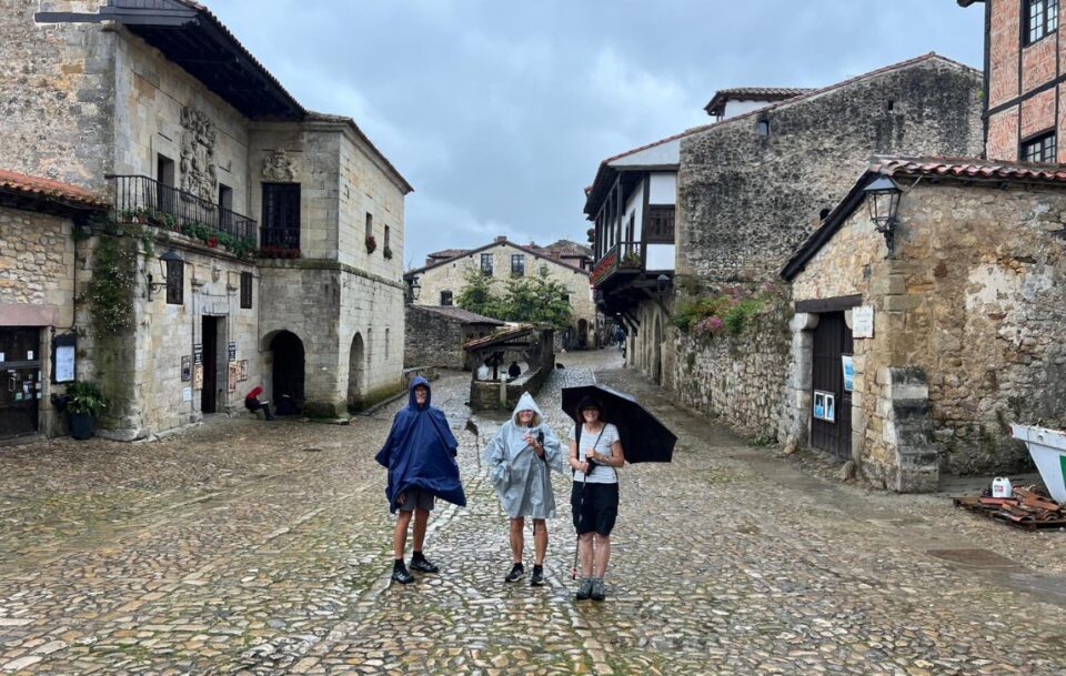 Three hikers huddled in the rain on a cobbled street in a Spanish village on the Camino del Norte