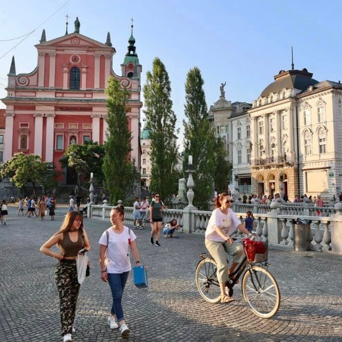 Tourists walking across a bridge in the compact and charming Slovenian capital city Ljubljana, with colourful Art Nouveau buildings in the background