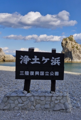 Japanese sign at Jodogahama Beach on the Michinoku Coastal Trail, with clear blue water and rocky shoreline in the background.