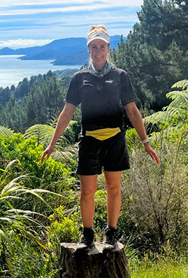 RAW Travel staff member Tamara on a lush green forest trail with New Zealand's Marlborough Sounds in the background.