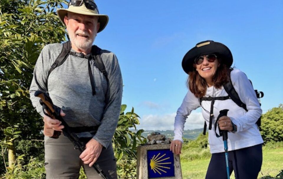 Two walkers on the Camino de Santiago next to a stone marker with the scallop shell.