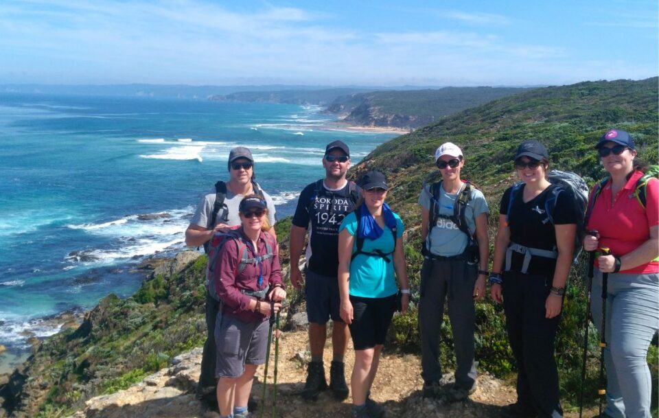 Group of happy hikers on a cliff top near Aire River on the Great Ocean Walk smiling at the camera.