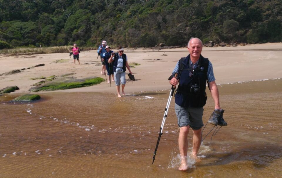 Barefoot hikers wading through the Parker River crossing on the Great Ocean Walk.