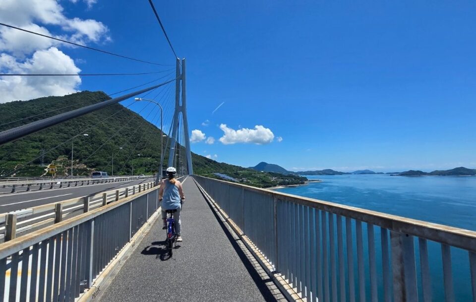 Person cycling across the Tatara Bridge on the Shimanami Kaido with the stunning blue Seto Inland Sea and islands in the background.