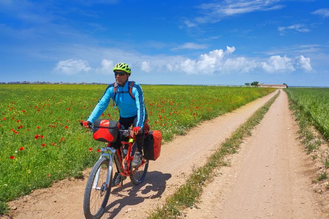 Cycling the Camino, Spain Man riding a bike along a dirt track on the Camino, with red poppies in the surrounding field.