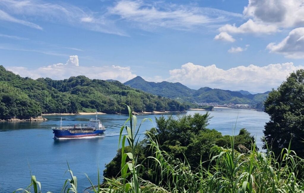 Large ship sailing on calm sea with forested mountains all around, Shimanami Kaido