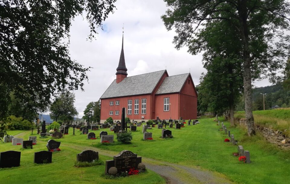 Red wooden church beside a cemetery in Norway.
