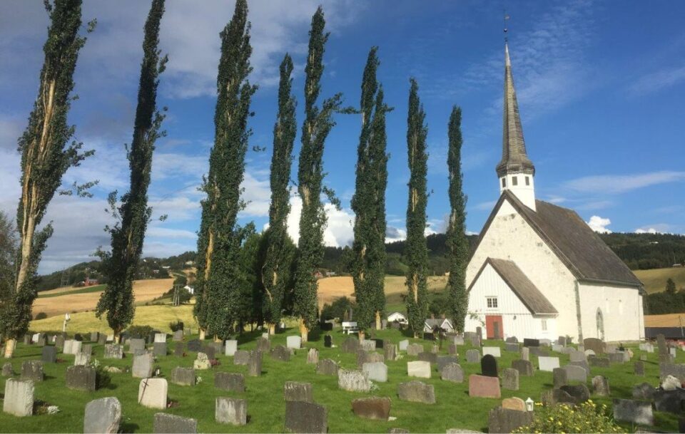 White wooden church with spire beside a cemetery in Norway.