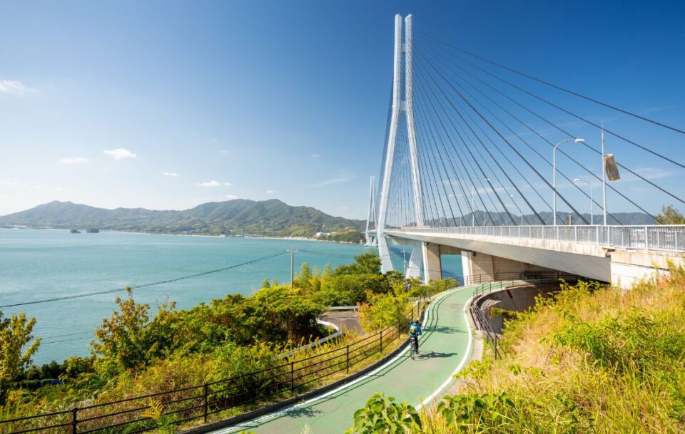 Cyclist approaching the Tatara Bridge on the Shimanami Kaido Cycling Route, Japan, with the cables fully visible.