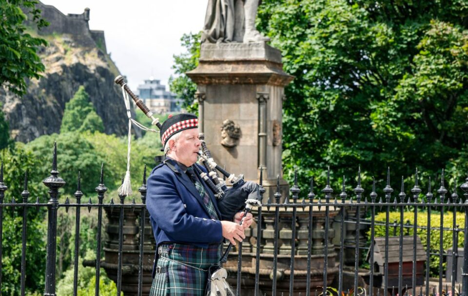 Scottish bagpiper performing outdoors in traditional kilt.