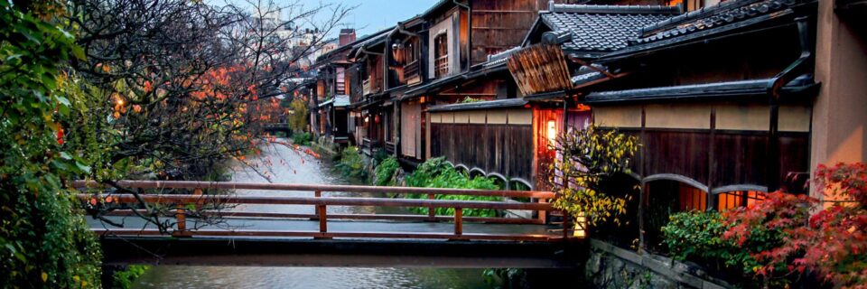 Historic wooden houses lining a street in Kyoto with a small pedestrian bridge over a canal.