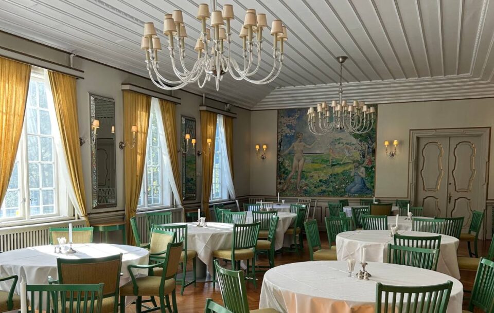 Elegant hotel dining room along St Olav’s Way featuring chandeliers, white tablecloths and candlesticks.