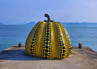 Bright yellow polka-dotted pumpkin sculpture by Yayoi Kusama on the shore of Naoshima Island, Japan.