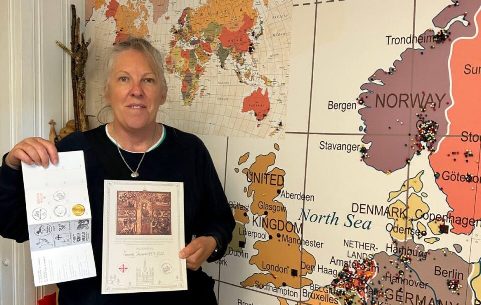 Pilgrim displaying her completion certificate and stamped passport in front of Norway map.