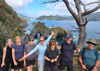 A group of happy hikers in front of the Anatoshi-iso Rock, a coastal landmark on Japan's Michinoku Coastal Trail