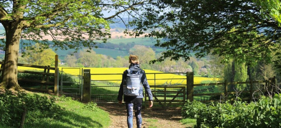 Female hiker approaching a gate that leads to the stunning green hills of the Cotswolds.