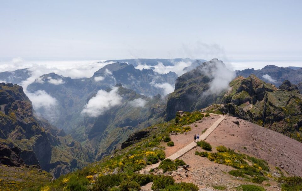 Hikers walking along the trail at Pico do Areeiro in the Madeira Islands with rugged mountain peaks and clouds.