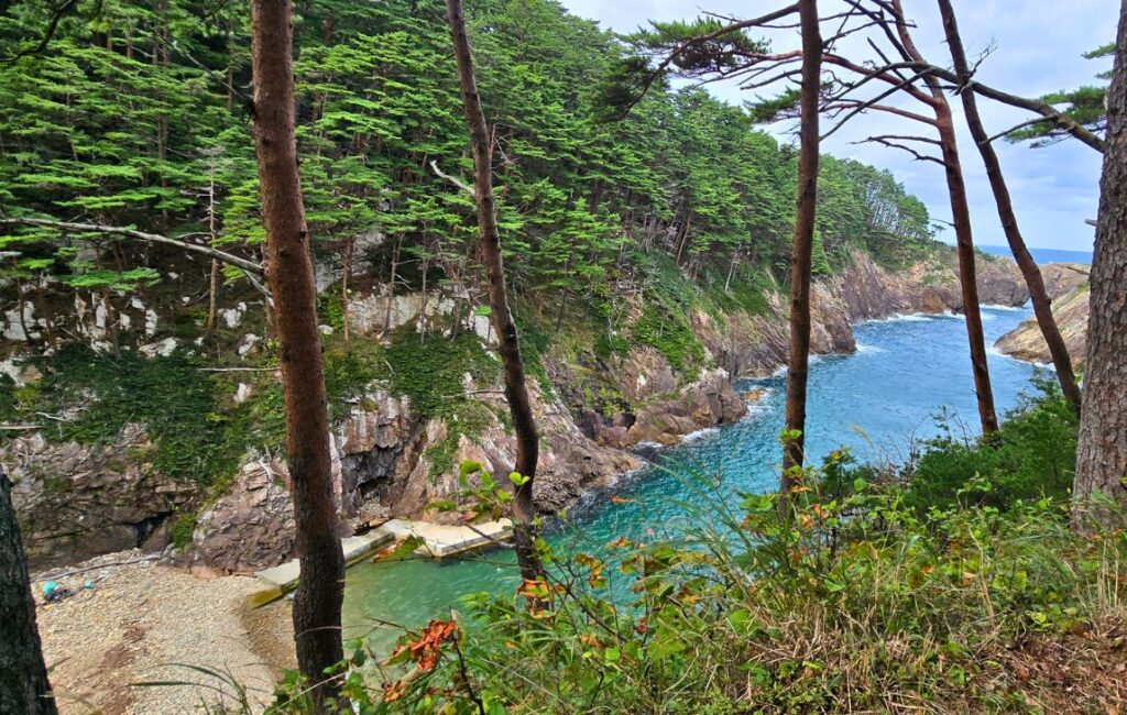 Scenic view of tree-covered cliffs dropping into clear turquoise water, Michinoku Coastal Trail.