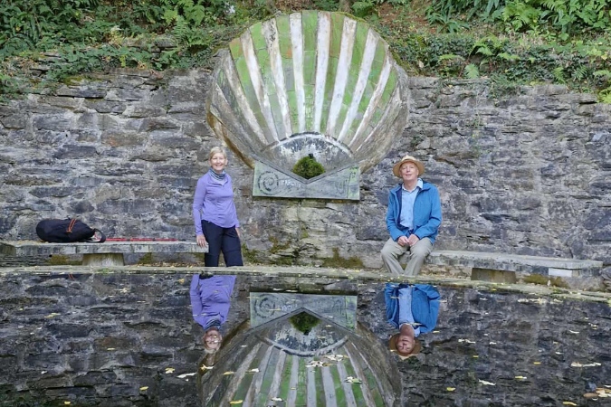 Hikers resting on a stone wall with a Camino shell reflected in water.