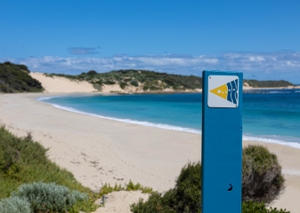 Blue wooden signpost on a beach beside turquoise water on the Cape to Cape Track.
