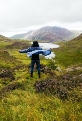 Hiker in the Lake District national park on the Coast to Coast Path with her back to camera, arms outstretched.