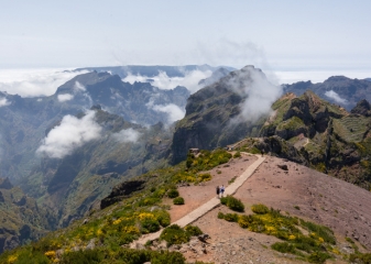 Hikers walking along the trail at Pico do Areeiro in the Madeira Islands with rugged mountain peaks and clouds.