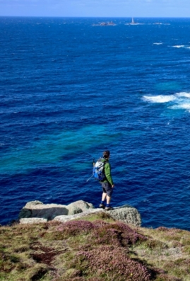 Scenic view of a hiker on a coastal rock with the ocean in the background, South West Coast Path, England.